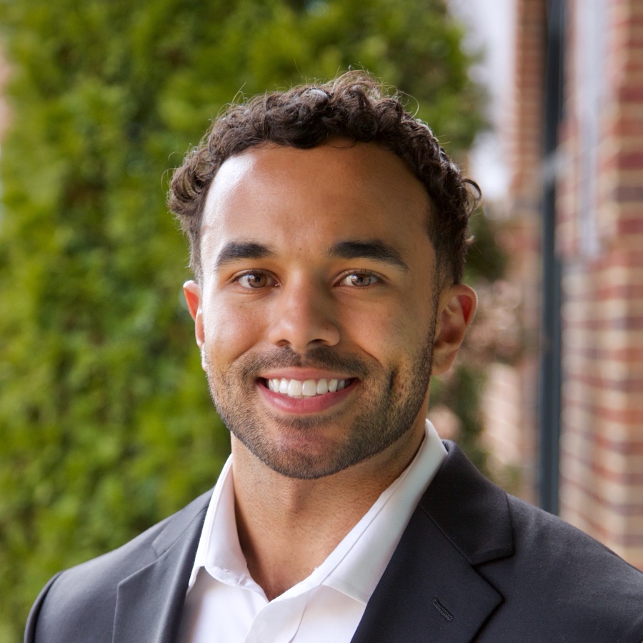 Micah Rock, smiling outside in a dark suit and white shirt